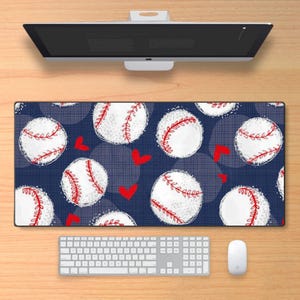 May include: A rectangular desk mat featuring a repeating pattern of white baseballs with red stitching and small red hearts on a dark blue background with a subtle grid texture. The mat is positioned below a computer monitor and keyboard.