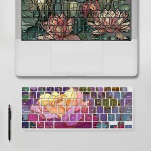 以下が含まれることがあります： ピンクとグリーンの蓮の花のデザインが施されたキーボードカバー付きのシルバーのノートパソコン。その下には、お揃いの花柄のワイヤレスキーボードが配置されており、ワイヤレスキーボードの左側には黒いスタイラスペンが置かれています。