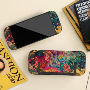 Może przedstawiać: Dwa etui na konsolę do gier z kolorowymi wzorami kwiatowymi. Jedno etui jest otwarte, wyświetlając ekran, a drugie zamknięte. Etui mają mieszankę różowych, niebieskich i żółtych wzorów kwiatowych z czarnymi przyciskami sterowania.