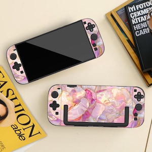 May include: Two Nintendo Switch consoles with matching decorative skins. The skins feature a pink, gold, and white floral pattern. One console is fully assembled, while the other shows the Joy-Con controllers and the screen separately.