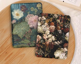 May include: Two rectangular e-reader cases featuring floral designs. The left case displays a white lotus and pink peonies on a teal background. The right case features a dense arrangement of multicolored flowers including white, red, and orange blooms on a black background.