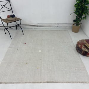 Puede incluir: Una alfombra rectangular blanca con una textura tejida sutil. La alfombra tiene un aspecto ligeramente desgastado con algunas marcas tenues.