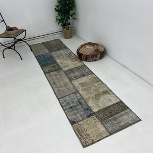May include: A long, rectangular patchwork rug with a variety of colors and patterns, including beige, brown, blue, and gray. The rug is made of recycled materials and has a distressed look.