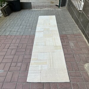 Pode incluir: Um tapete retangular branco com um design de patchwork. O tapete é feito de diferentes tons de branco e bege.