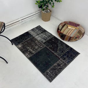 Puede incluir: Una alfombra de patchwork negro y gris con un aspecto desgastado. La alfombra está hecha de diferentes piezas de tela cosidas juntas. Es una gran adición a cualquier hogar.