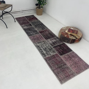 May include: A long, rectangular runner rug with a patchwork design in shades of gray, brown, and burgundy. The rug is made of woven fabric and has a distressed, vintage look.