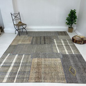 May include: A patchwork rug with a variety of colors and textures, including gray, brown, and white. The rug is made up of different pieces of fabric that have been sewn together.