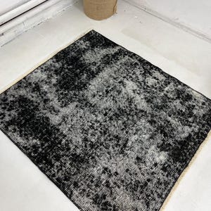 Puede incluir: Alfombra desgastada en blanco y negro con un aspecto descolorido y vintage. La alfombra tiene un patrón sutil y una textura suave y desgastada.