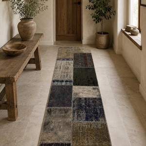 Puede incluir: Una alfombra rectangular de patchwork con un aspecto envejecido y vintage. La alfombra presenta una variedad de colores apagados, incluyendo beige, gris, azul marino y verde oliva, dispuestos en un patrón geométrico. La alfombra está colocada en un pasillo.