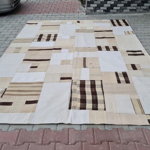 May include: A large, rectangular patchwork rug with a white background and brown and beige geometric patterns. The rug is made of different pieces of fabric sewn together.