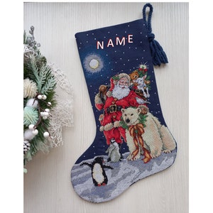 May include: A blue Christmas stocking with a white polar bear, penguins, and Santa Claus with a sack of gifts. The stocking has a white moon and stars on a dark blue background. The stocking has the word "NAME" embroidered on the top.