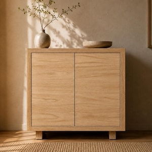 May include: A light-colored wooden cabinet with two doors. A small, round vase with a plant and a wooden bowl sit on top. The cabinet is on a woven rug.