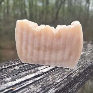 Puede incluir: Una barra de jabón marrón claro con una superficie texturizada. El jabón está sobre una superficie de madera desgastada.