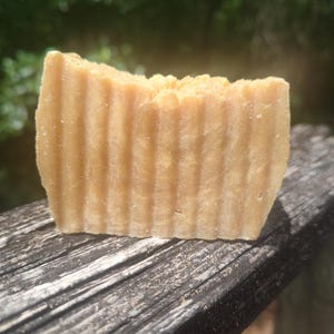 May include: A bar of handmade soap with a light brown color and a rippled texture. The soap is sitting on a wooden surface.