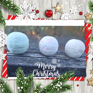 Könnte beinhalten: Drei Badebomben in einem Weihnachtsbild. Die Badebomben sind weiß, hellblau und weiß mit rosa Wirbeln. Der Text "Frohe Weihnachten" ist auf einer Holzoberfläche geschrieben.