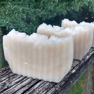 May include: Three bars of white soap with a textured surface. The soap bars are arranged in a row on a wooden surface.
