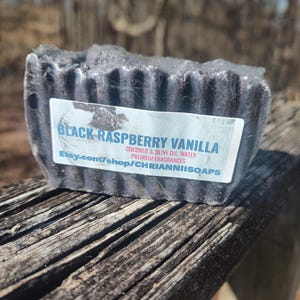 May include: Black Raspberry Vanilla soap bar with a black and white label that reads "Black Raspberry Vanilla Coconut & Olive Oil, Water Premium Fragrances Etsy.com/shop/CHRIANNIISOAPS"