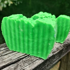 May include: Two green bars of soap with a striped pattern. The soap is on a weathered wooden surface.
