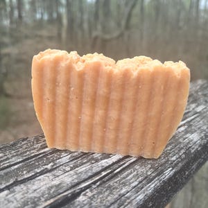 May include: A bar of handmade soap with a light brown color and a ridged texture. The soap is sitting on a weathered wooden surface.
