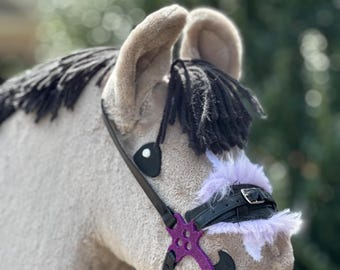 May include: A gray and white stuffed horse head with black mane and tail. The horse is wearing a black leather bridle with a purple snaffle bit.