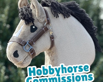 May include: A plush hobby horse head in beige with a dark brown mane and a brown bridle. The horse has black eyes and a white stripe down its face. The text "Hobbyhorse Commissions" is displayed in a teal font.
