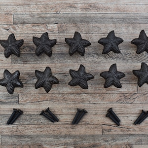 May include: Twelve black cast iron starfish drawer pulls with screws. The pulls are arranged in two rows of six on a wood surface.
