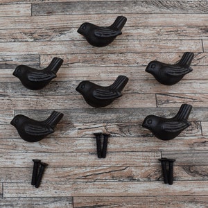 May include: Six black cast iron bird-shaped drawer pulls with a rustic finish. The pulls are arranged in a pattern on a wooden surface. Three screws are also included.