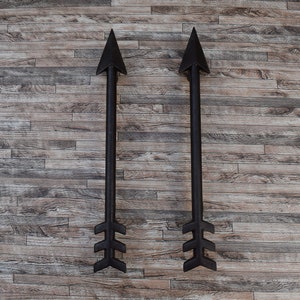 May include: Two black metal arrows with fletching pointing upwards against a woodgrain background.