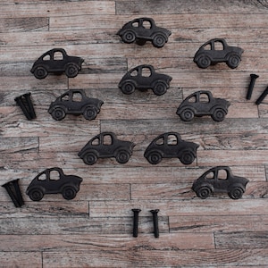 May include: Ten black cast iron car-shaped drawer pulls with screws on a wood background.