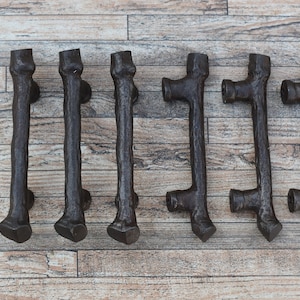 Może przedstawiać: Osiem rustykalnych brązowych metalowych gałek do szafek w kształcie gałęzi. Gałki mają szorstką, fakturowaną powierzchnię i są zaprojektowane tak, aby przypominały naturalne drewno.