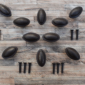 May include: Ten black oval cabinet knobs with a distressed finish and twelve black screws on a wood background.