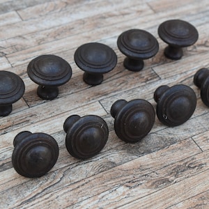 Op de afbeelding: Twaalf zwarte metalen kastknoppen met een rond ontwerp en een verhoogde rand. De knoppen zijn in twee rijen op een houten oppervlak gerangschikt.