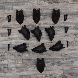Puede incluir: Diez ganchos de cabeza de lobo de hierro fundido negro con tornillos sobre un fondo de madera.