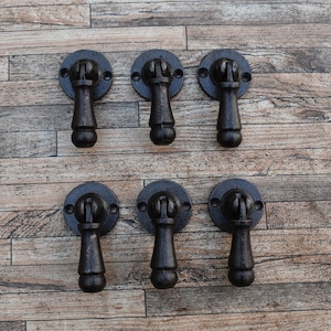 May include: Six black cast iron drawer pulls with a round base and a loop handle. The pulls are arranged in two rows of three on a wood background.