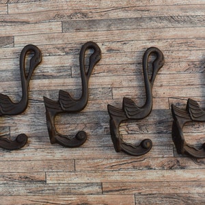 May include: Four wooden swan-shaped hooks, each with a curved neck and a rounded base. The hooks are dark brown and have a rustic finish. They are mounted on a wooden wall.