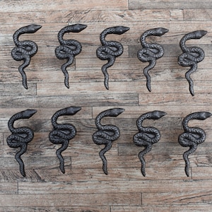 Puede incluir: Doce tiradores de puerta de serpiente de hierro fundido negro con tornillos. Los tiradores de serpiente están en posición en espiral con la cabeza en la parte superior.