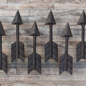 May include: Eight black metal arrow-shaped wall decor pieces arranged in a row on a woodgrain background.