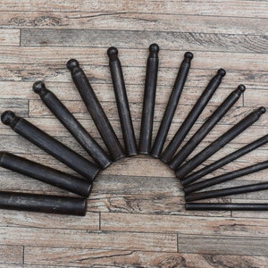 Könnte beinhalten: Ein Satz von 18 schwarzen Lederwerkzeugen aus Metall mit abgerundeten Spitzen, die in einem Halbkreis auf einer Holzoberfläche angeordnet sind.