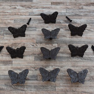 Peut inclure: Neuf poignées de tiroir en forme de papillon en fonte noire avec vis sur un fond en bois.