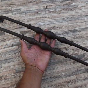 Può includere: Due maniglie per porte in metallo marrone scuro. Ogni maniglia ha un'estremità curva e una sezione centrale decorativa. Le maniglie sono mostrate su uno sfondo a venature di legno. Le maniglie sono lunghe circa 30 cm.