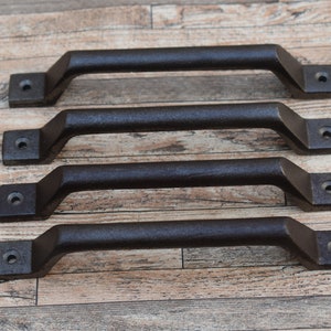 Può includere: Quattro maniglie in metallo marrone scuro, di forma rettangolare e con finitura strutturata. Ogni maniglia ha una base rettangolare con un foro per il montaggio. Le maniglie sono distanziate e disposte orizzontalmente.