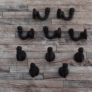 May include: Nine black metal hooks with a rounded top and a curved hook. The hooks are arranged in three rows on a wooden surface.