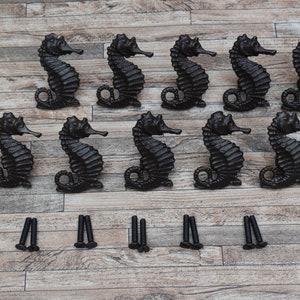 May include: Ten black cast iron seahorse drawer pulls with screws. The pulls are about 3 inches tall and 2 inches wide.
