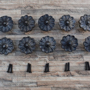 以下が含まれることがあります： 木製の表面に、花柄の黒い金属製の引き出しノブが12個、2列に6個ずつ並んでいます。ノブには黒いネジが12本付属しています。