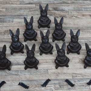 May include: Ten black cast iron rabbit figurines on a woodgrain surface. The rabbits are all in a sitting position with their ears upright.