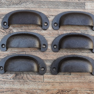 May include: Six black metal drawer pulls with a rounded, slightly curved shape. The pulls have a distressed finish and are arranged in two rows of three.