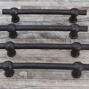 Puede incluir: Cuatro tiradores de cajón de metal negro con extremos redondeados. Los tiradores están dispuestos en una fila sobre una superficie de madera.