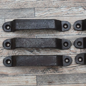 May include: Five black metal drawer pulls with rounded edges and a distressed finish. Each pull has two holes for mounting.