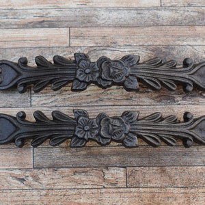 Può includere: Due tiretti per cassetti in metallo nero con decorazioni floreali ornate. I tiretti hanno un design a forma di cuore a ciascuna estremità e sono decorati con foglie e fiori.