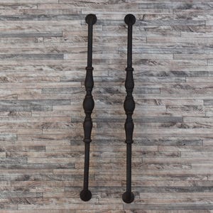 Puede incluir: Dos barras de metal verticales negras y ornamentadas con detalles decorativos. Cada barra tiene una parte superior e inferior redondeadas, y una serie de formas bulbosas a lo largo de la longitud. Las barras están sobre un fondo de tablones de madera marrón claro y gris.